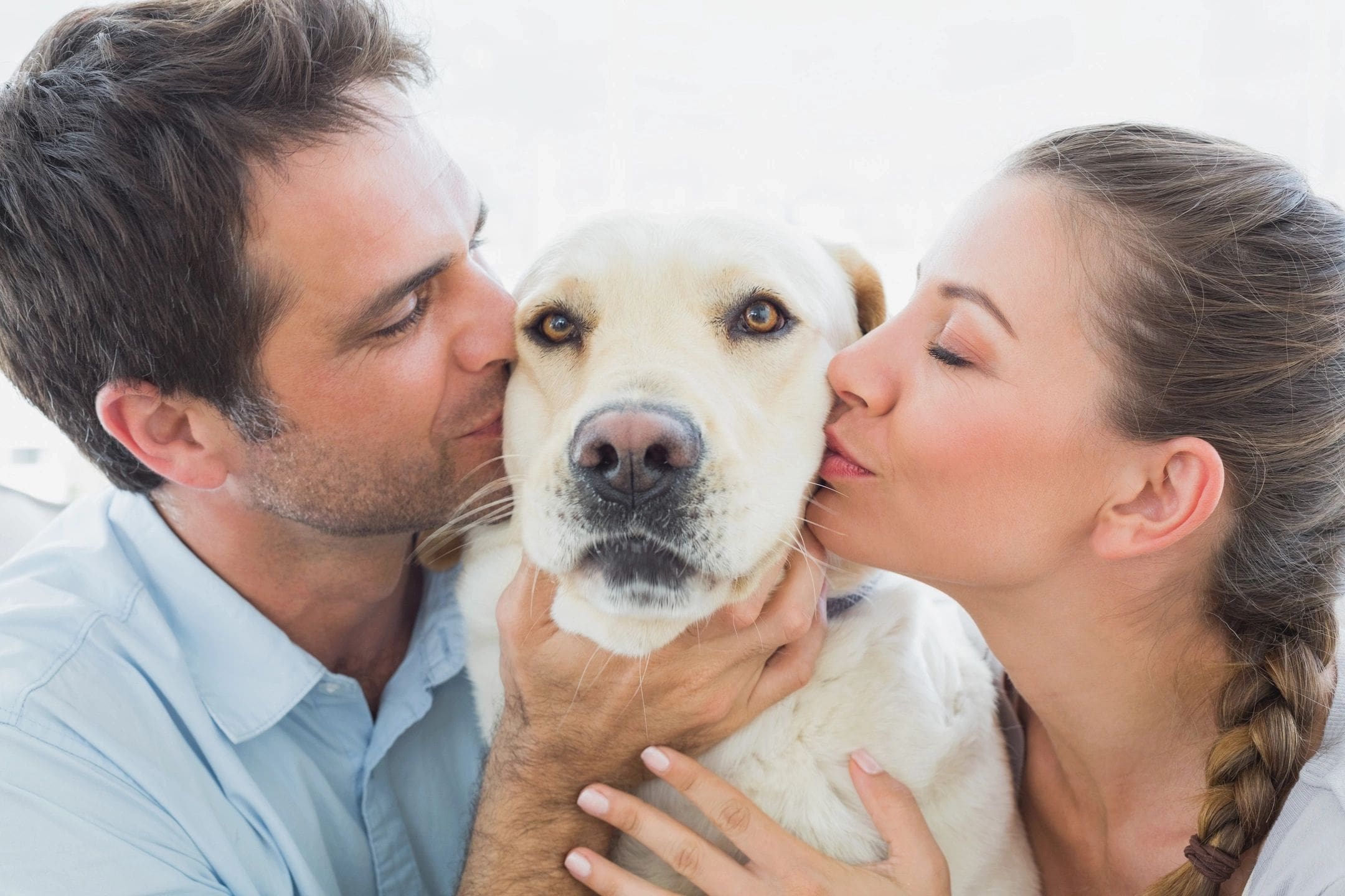 A man and woman kissing their dog.